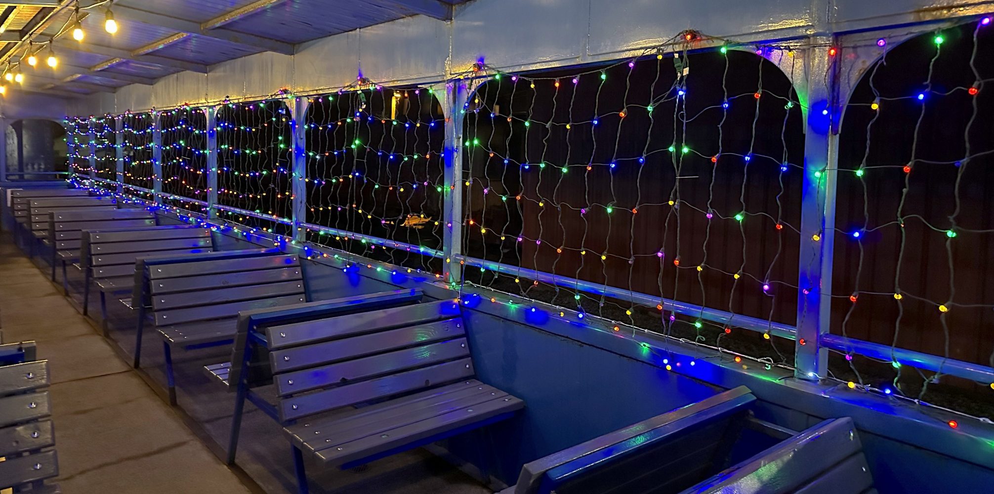 Empty ferry deck with string lights hanging on the windows and benches arranged in rows.
