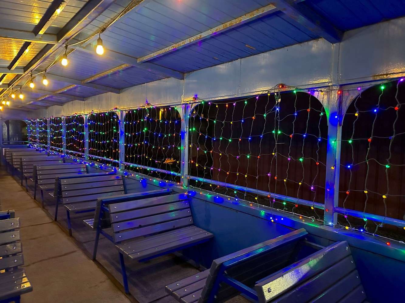 Empty ferry deck with string lights hanging on the windows and benches arranged in rows.