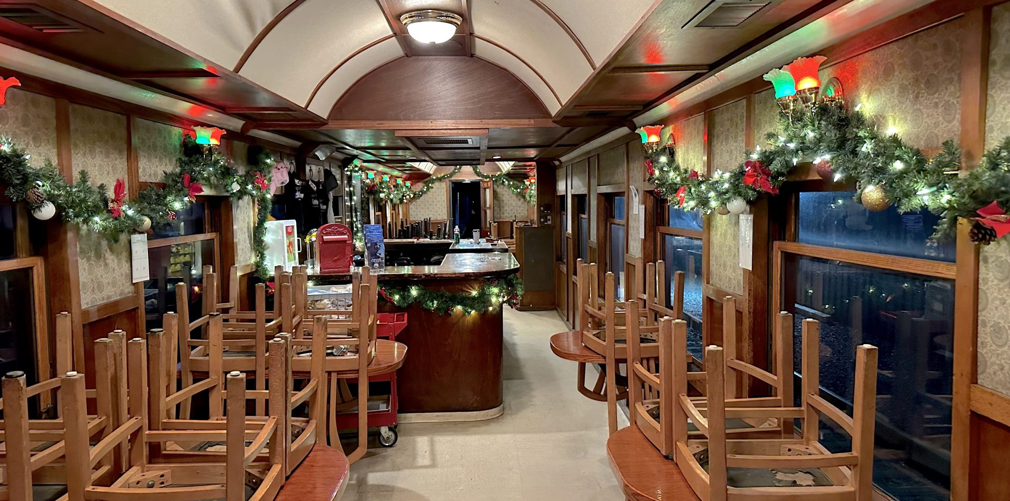 Train dining car with holiday decorations and chairs stacked on tables.