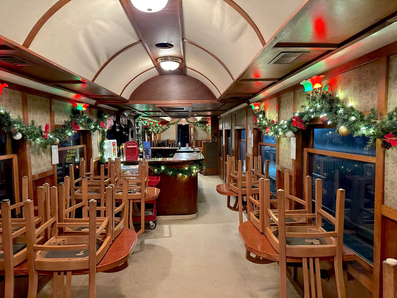 Train dining car with holiday decorations and chairs stacked on tables.