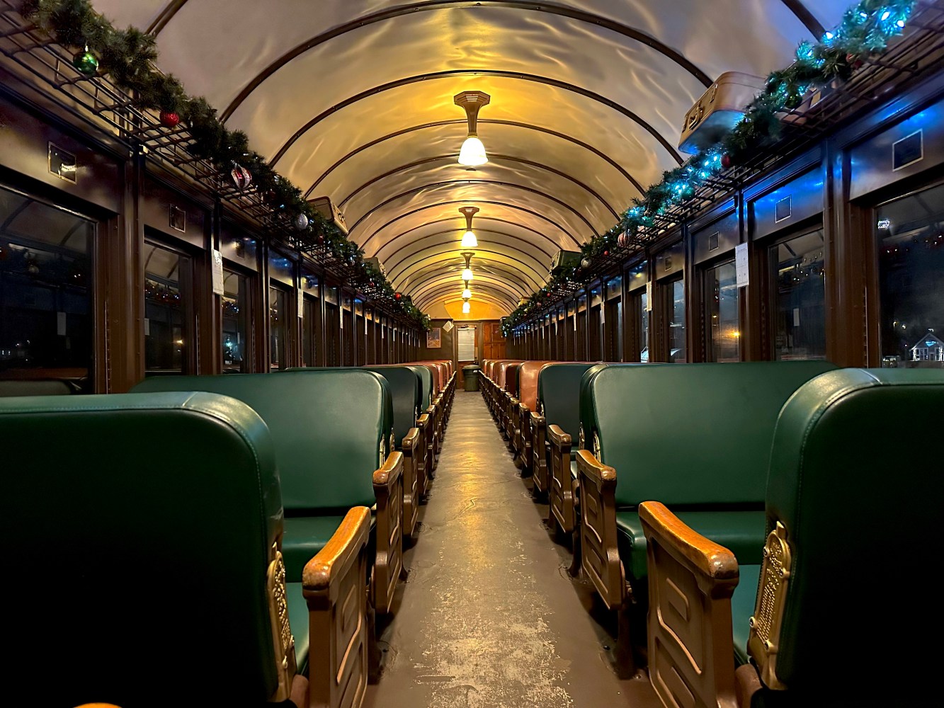 Decorated vintage train interior with green seats and ceiling garlands.