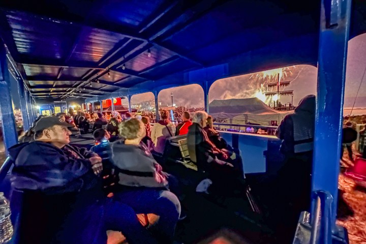 People sitting inside a blue train carriage, watching fireworks through the open windows.