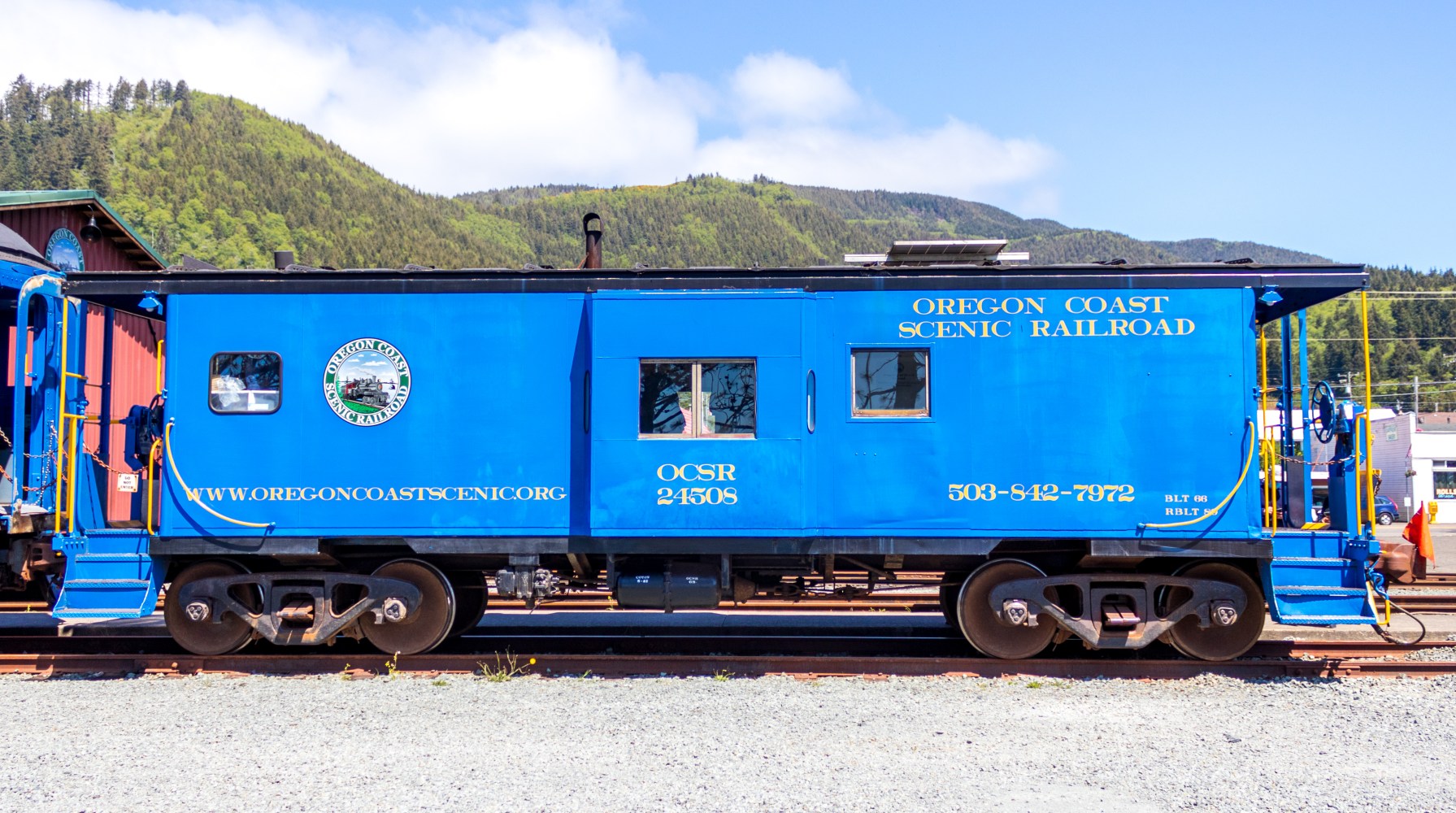 Blue Oregon Coast Scenic Railroad train car on tracks with mountains in background.