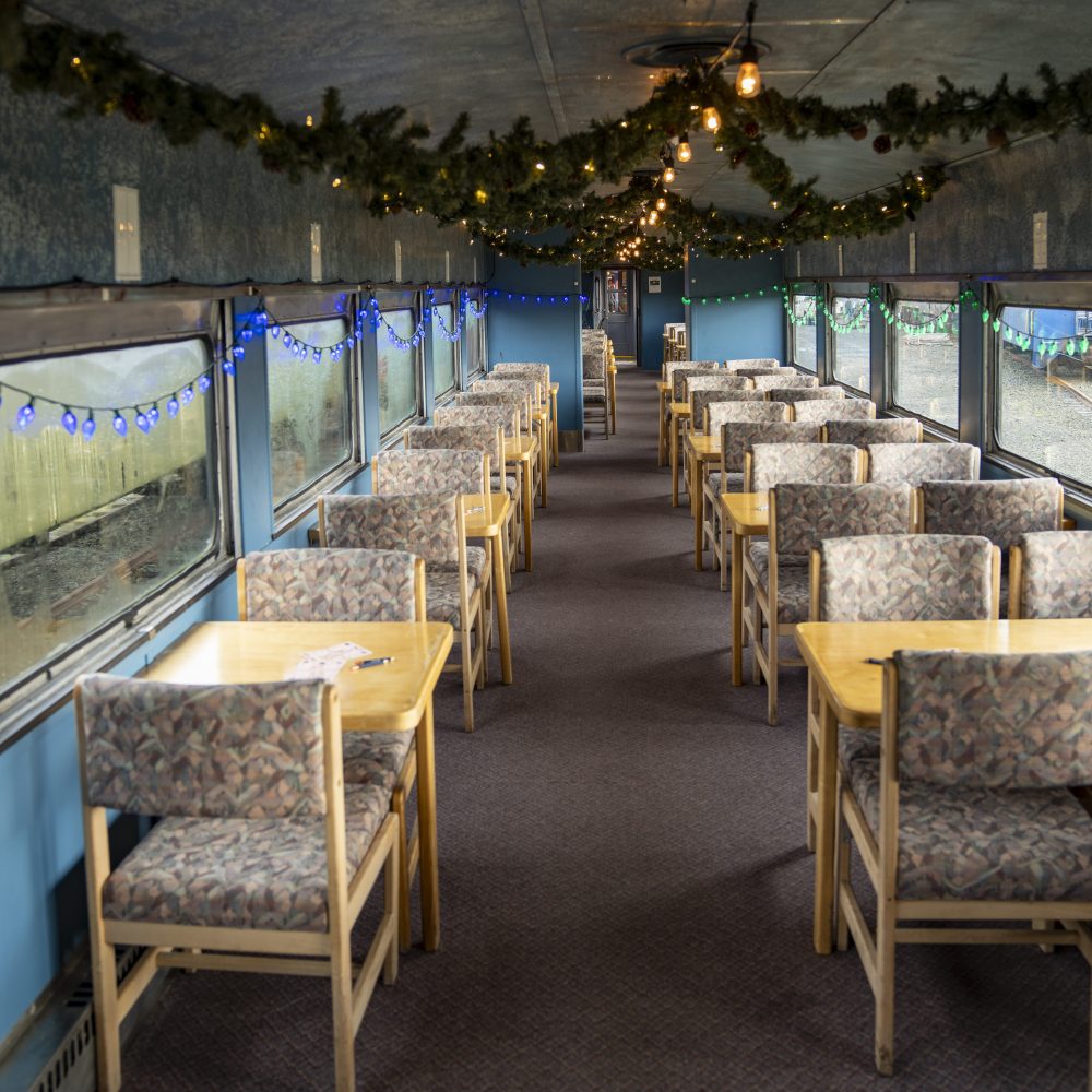 Decorated train car with tables, chairs, string lights, and garlands.