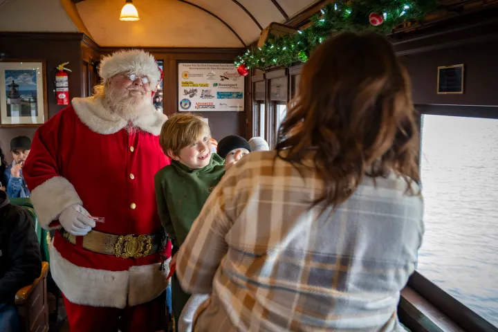 Santa Claus interacting with smiling child on a train decorated with festive garland.