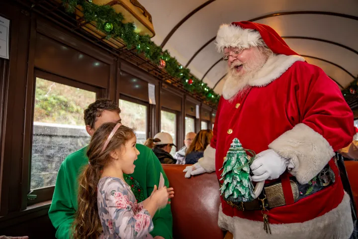 Santa Claus talking to a smiling child on a festive train.