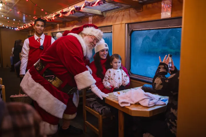 Santa greets a family on a festively decorated train.