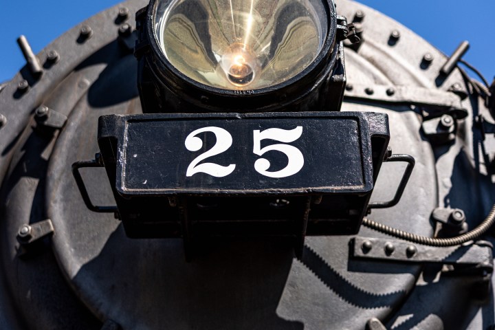 Steam train engine front with number 25, large headlight, and blue sky background.