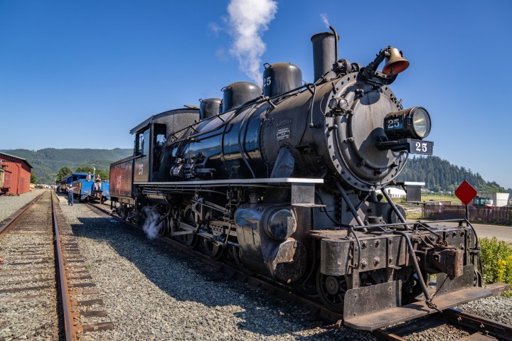 Vintage steam locomotive numbered 25 on train tracks under a clear blue sky.