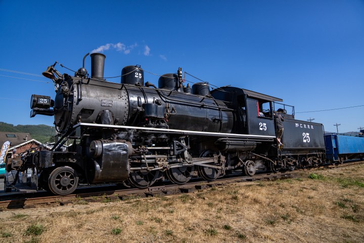 Black steam locomotive engine on tracks under a clear blue sky.